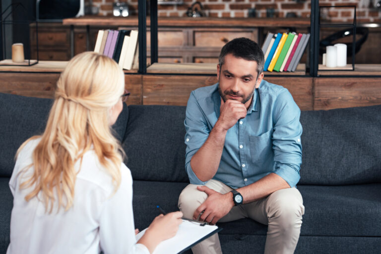 female therapist writing in clipboard and talking to male patient in office