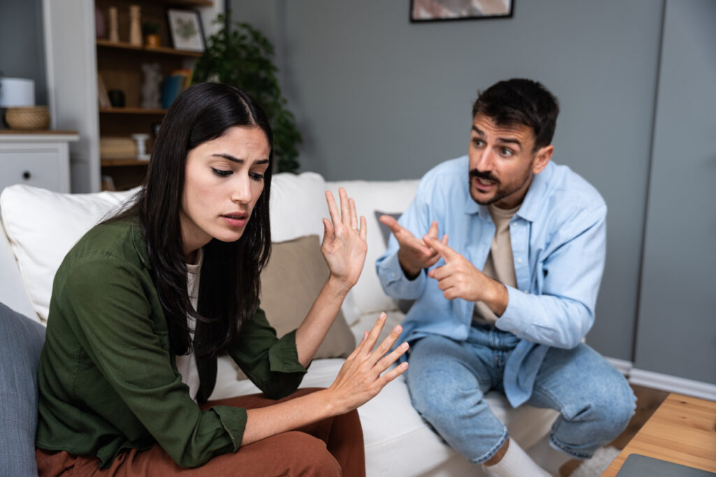 Couple experiencing a tense argument at home, with one partner gesturing while the other withdraws