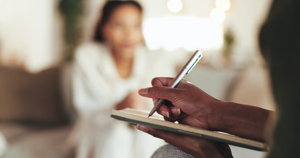 close up of a therapists hands writing on a notepad with patient in the background