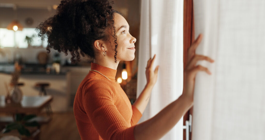 smiling woman looking moving curtains to look out of the window