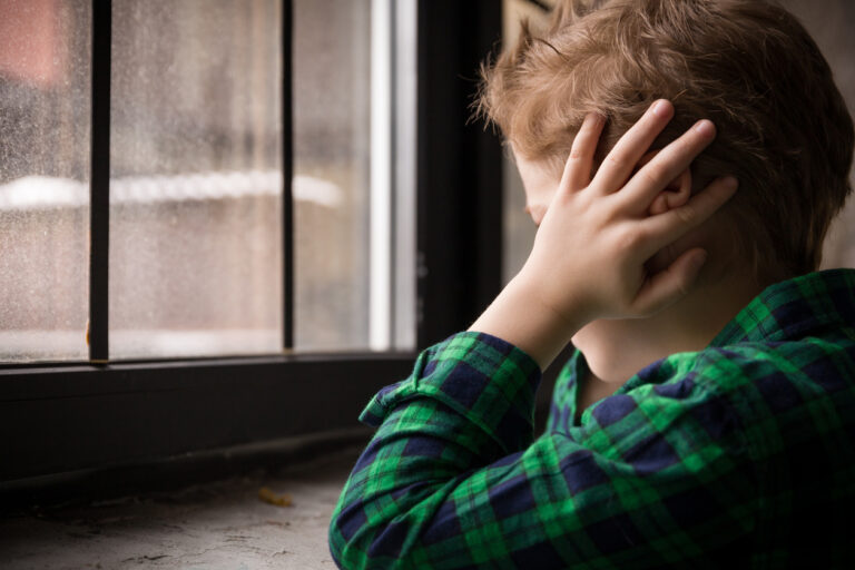 Little boy standing by the window in sad mood.