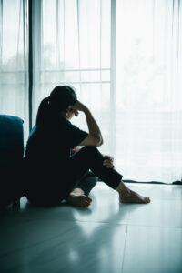 woman sits on the floor by window with hand on head